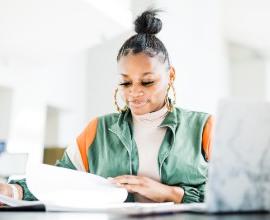 Female student studying with notes and laptop.